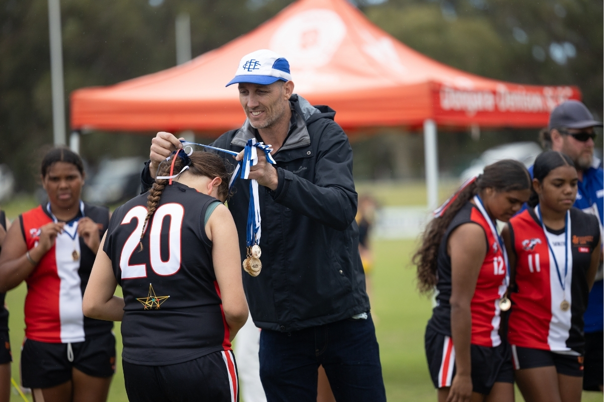 AFL great and local legend, Harry Taylor presenting premiership medals to the Mullewa Saints Youth Girls team, photographed by Jesse Pickett 